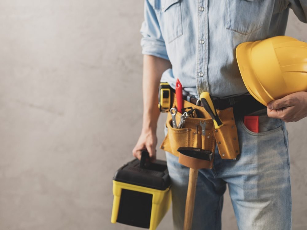 Worker man holding construction helmet and toolbox near wall. Male hand and tools for house room renovation. Home renovation concept